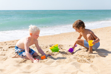 Children two little boys playing on the beach on summer holidays. Children have fun, build sand...