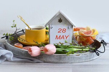 Calendar for May 28: numbers 28, name of the month May in English, tray with cup of tea and...