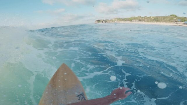 Surfer rides on ocean wave at Balangan surf spot in Bali island, action camera first person view