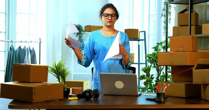 Indian Asian small businesswoman holding order list celebrating success with joyful expression after receiving large number of online product orders or shipment confirmation standing at store room
