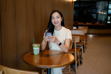 Young asian woman using mobile phone while drinking beverage at cafe
