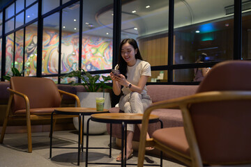 Young Asian businesswoman using smartphone and relaxing on sofa in modern cafe