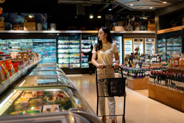 Customer pushing shopping cart and choosing frozen food in supermarket