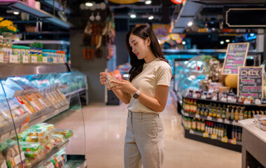 Young woman checking nutrition facts of packaged food in supermarket refrigerator shelves
