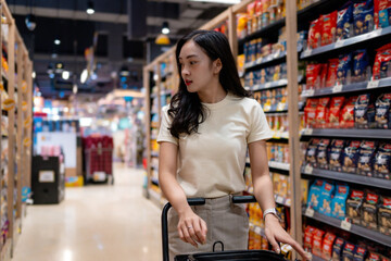Customer pushing shopping cart and choosing snacks in supermarket