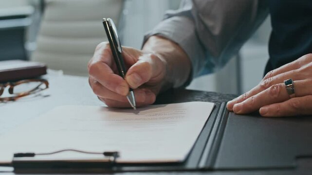 Close up shot of hands of unrecognizable businessman signing contract at table in office