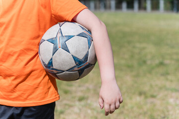 Close-up of soccer ball held under male arm outdoors.