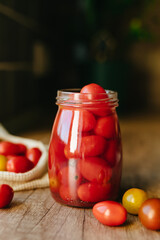 Pickled cherry tomatoes in a glass jar on the wooden table