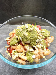Shrimp salad with pesto and cashews in glass bowl on stone surface
