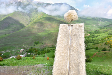 A white Caucasian papakha and burka against the background of green Caucasian mountains. View of Caucasian sheepskin clothing against the background of mountains on a sunny summer day.