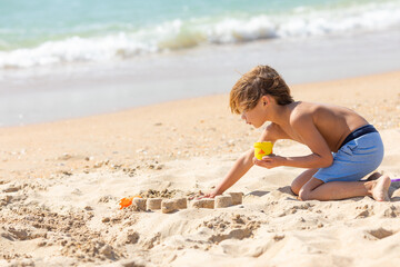 Side view child little boy playing with the sand on the beach, building sand castle, enjoying summer, playing. Advertising for tour operators, hotels, airlines. Vacation concept.