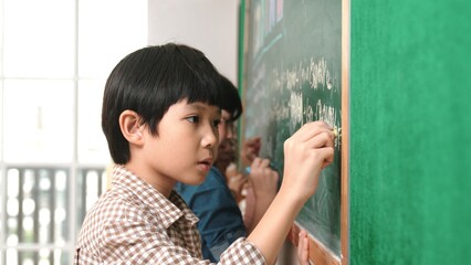 Side view of asian boy writing engineering prompt and programing system while standing blackboard...