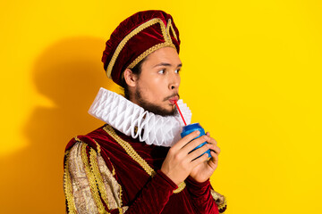 Young man dressed as a medieval nobleman sipping a drink against a vibrant yellow background