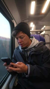 A young person is completely absorbed in their mobile phone while traveling on the train