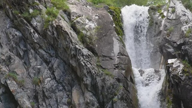 Slow motion footage of a breathtaking waterfall in Himachal Pradesh resembling the stunning Rutor Waterfalls in Italy. The cascading water flows over rocky terrain, surrounded by lush greenery.