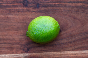 A whole green lime on a wood cutting board