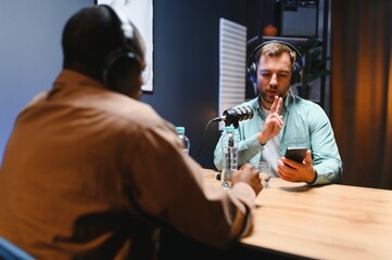 Show host and guest meeting to stream podcast episode together, creating online content with live broadcast discussion. Vlogger talking to man using professional equipment to record chat