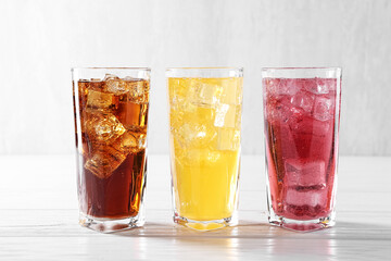 Soda water of different flavors with ice cubes in glasses on white wooden table