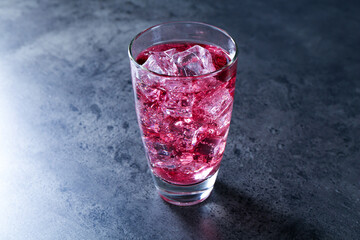 Sweet soda water with ice cubes in glass on grey table