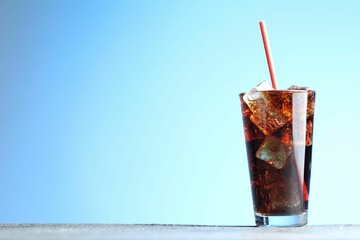Refreshing cola with ice cubes and straw in glass on grey textured table against light blue gradient background, closeup. Space for text