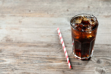 Refreshing cola with ice cubes in glass and straw on wooden table. Space for text