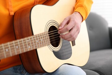 Fototapeta premium Young man playing guitar on sofa indoors, closeup