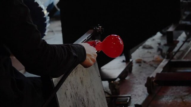 Glassblower at work with hot glass using a blowpipe and melting in an oven. 