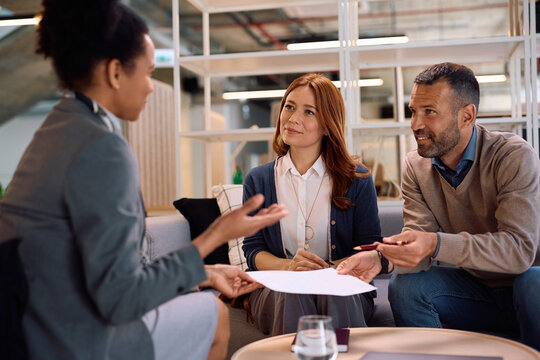 Happy couple and their financial advisors tough through terms of a contract before signing it in the office.