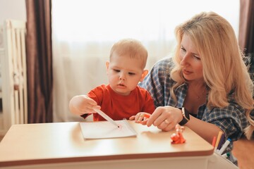 Mother helping little son drawing with colored pencils on notebook