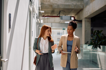Black businesswoman and her female colleague talking while walking through office hallway.