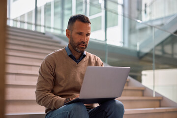 Fototapeta premium Corporate manager using laptop on staircase of office building.