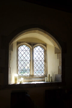  church window with three white candles on each side of the window on the window ledge above and below the window the wall is black, ideal for copy space, Parish church,  East Sussex, United Kingdom