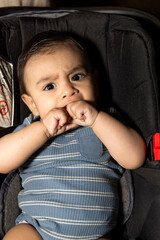 baby in stroller with angry face sucking both hands