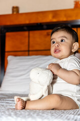 baby sitting on a bed making a weird face while holding a stuffed animal