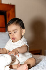 Baby sitting on a bed trying to reach a stuffed animal and the baby has his mouth open