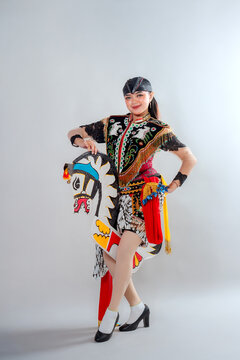 A female Jathilan dancer poses gracefully in traditional Javanese attire, holding a flat horse puppet with intricate patterns, representing Indonesian cultural heritage and folklore performance.