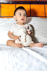 Baby sitting on bed with a scared face, clutching his stuffed animal