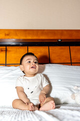 Baby sitting in bed looking up, already fed up with everything around him