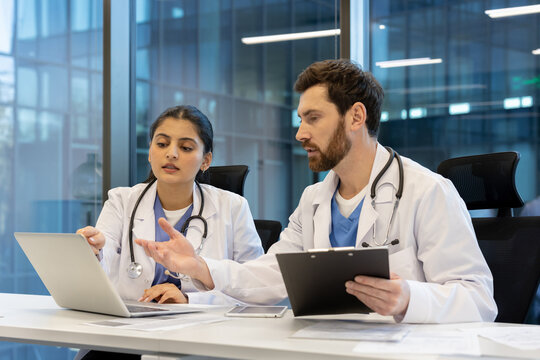 Two medical professionals collaborate, discussing information displayed on a laptop in a modern office setting. They are reviewing data together.