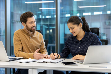 A man and a woman are collaborating in an office setting, with the woman signing documents. They appear to be reviewing a report.