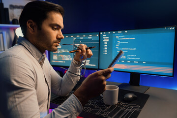 Smart IT developer working on software development coding on pc screen and reading note of newest...