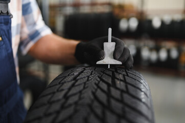 Mechanic measuring tire tread depth in automobile service centre