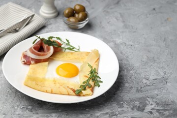 Delicious crepe bretonne with bacon and arugula on grey textured table. Space for text