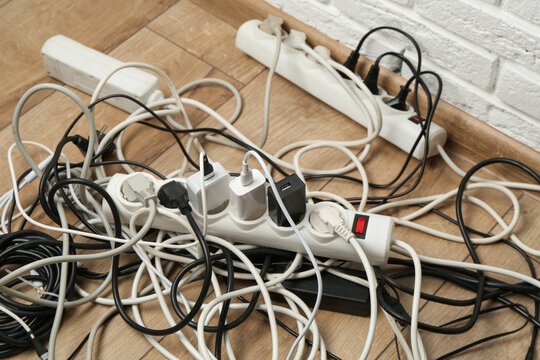 Extension power boards overloaded with plugs on wooden floor, closeup