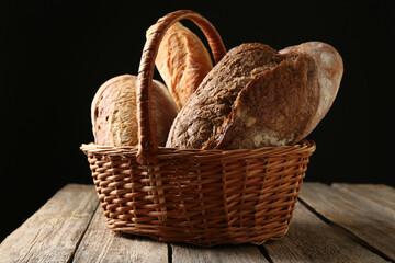 Different loaves of fresh bread in basket on wooden table, closeup