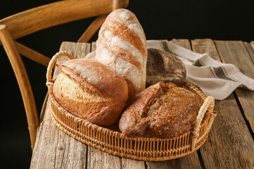 Different loaves of fresh bread in basket on wooden table