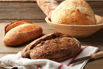 Different loaves of fresh bread and knife on wooden table, closeup
