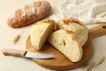 Different types of fresh bread, knife and spikelets on light textured table, closeup