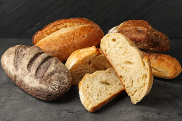 Different types of fresh bread on dark textured table against black background, closeup