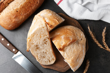Different types of fresh bread, spikelets and knife on dark textured table, flat lay